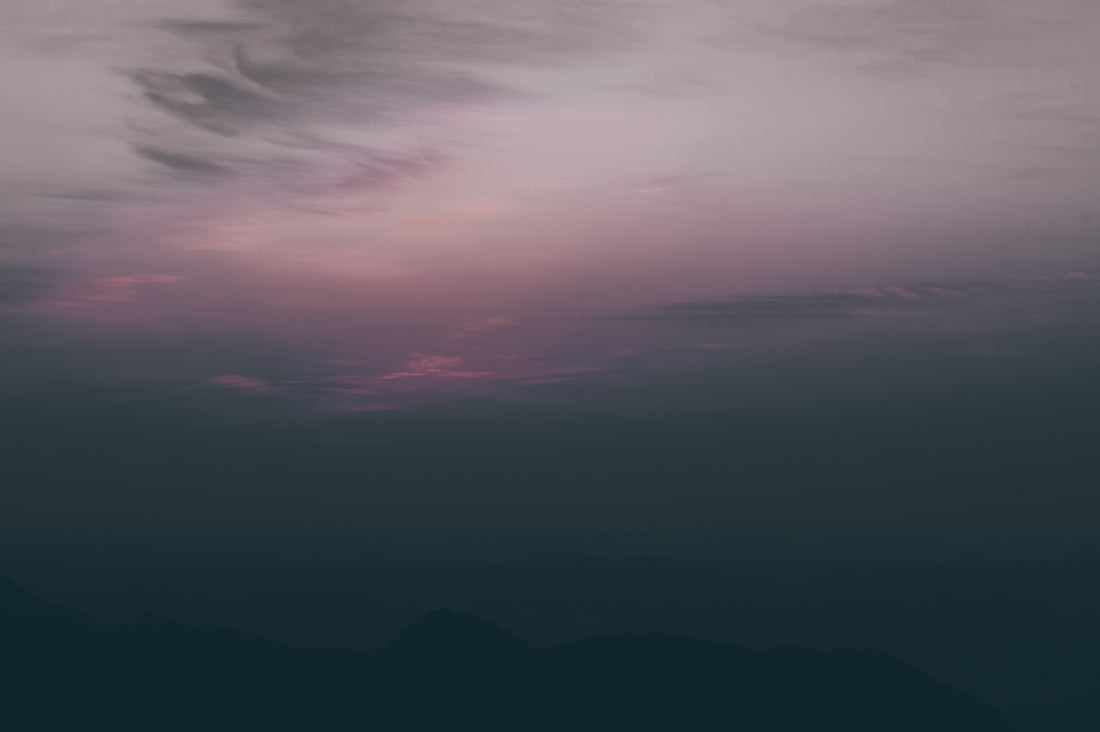 a plane flying through a cloudy sky with mountains in the background