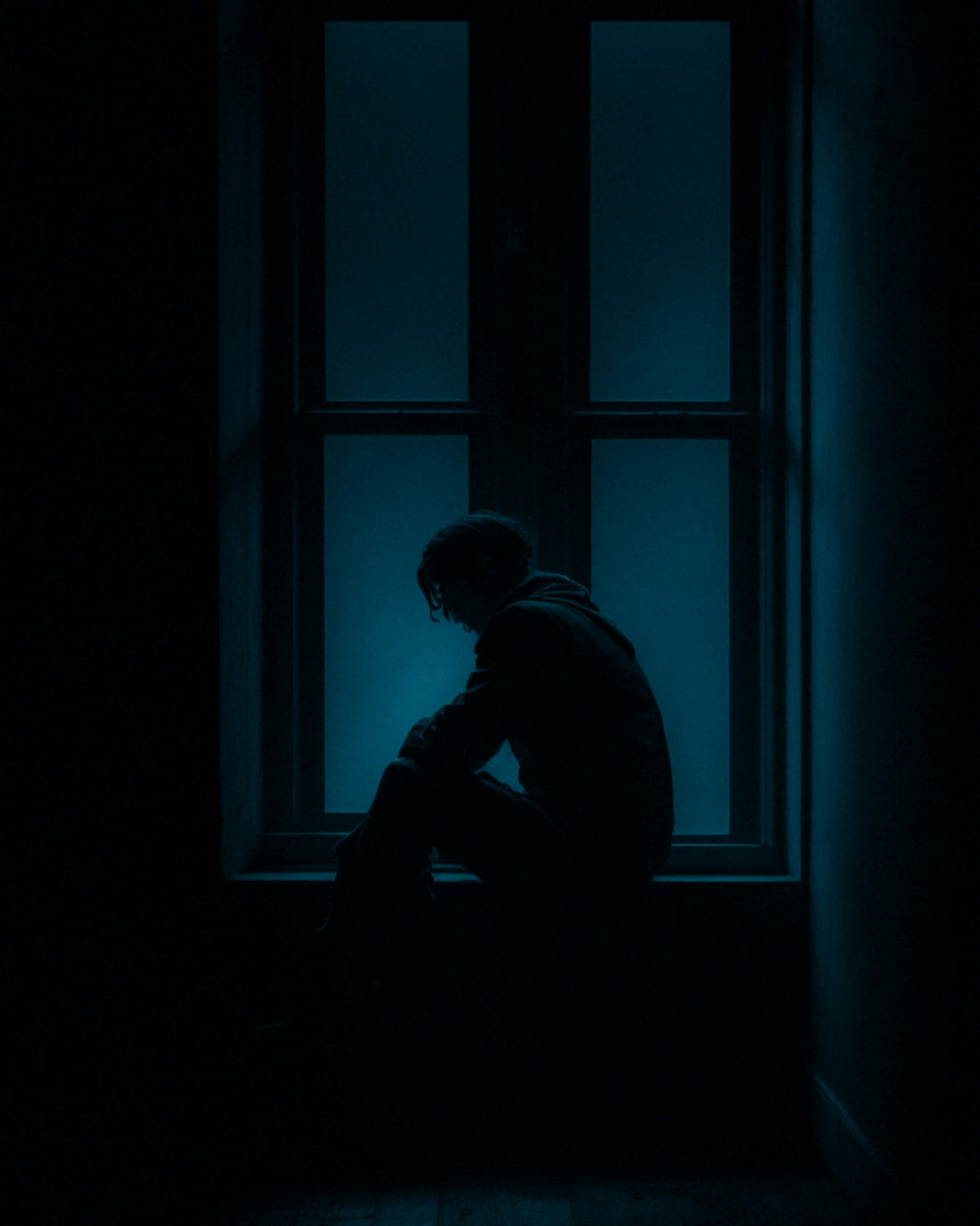 a man sitting on a window sill in the dark