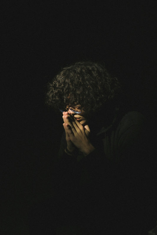 A person covers their face in the dark.