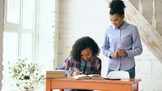 Woman helps girl with homework at desk.
