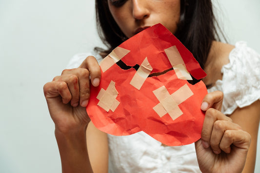 Woman holding a broken heart repaired with bandages.